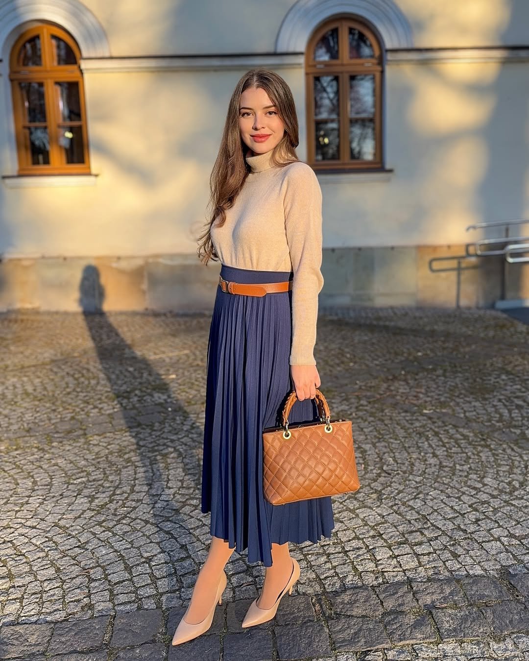 Beige Fine-Knit Turtleneck with Pleated Navy Midi Skirt and Tan Quilted Handbag