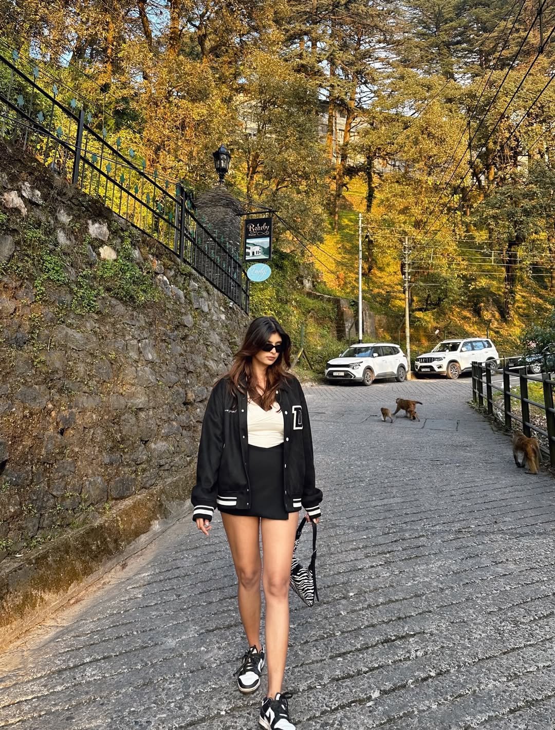 Black Varsity Bomber Jacket with Cream Top, Pleated Skort, and Zebra Print Shoulder Bag