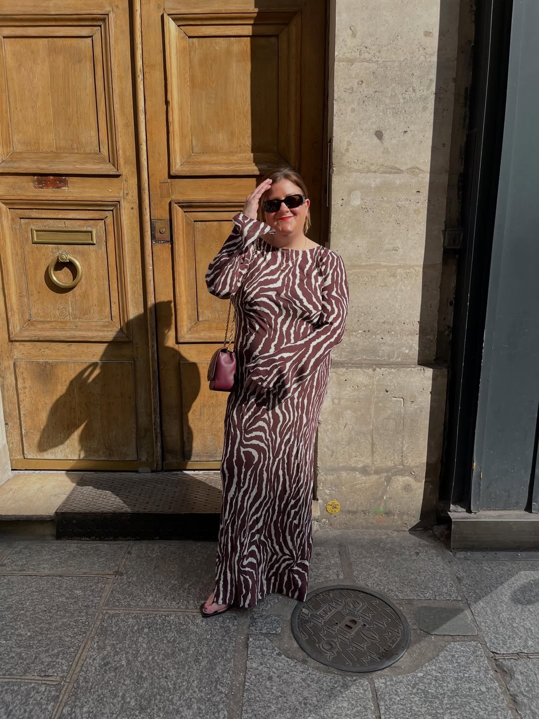 Brown Zebra-Print Maxi Dress with Burgundy Chain Bag against Paneled Wood Door