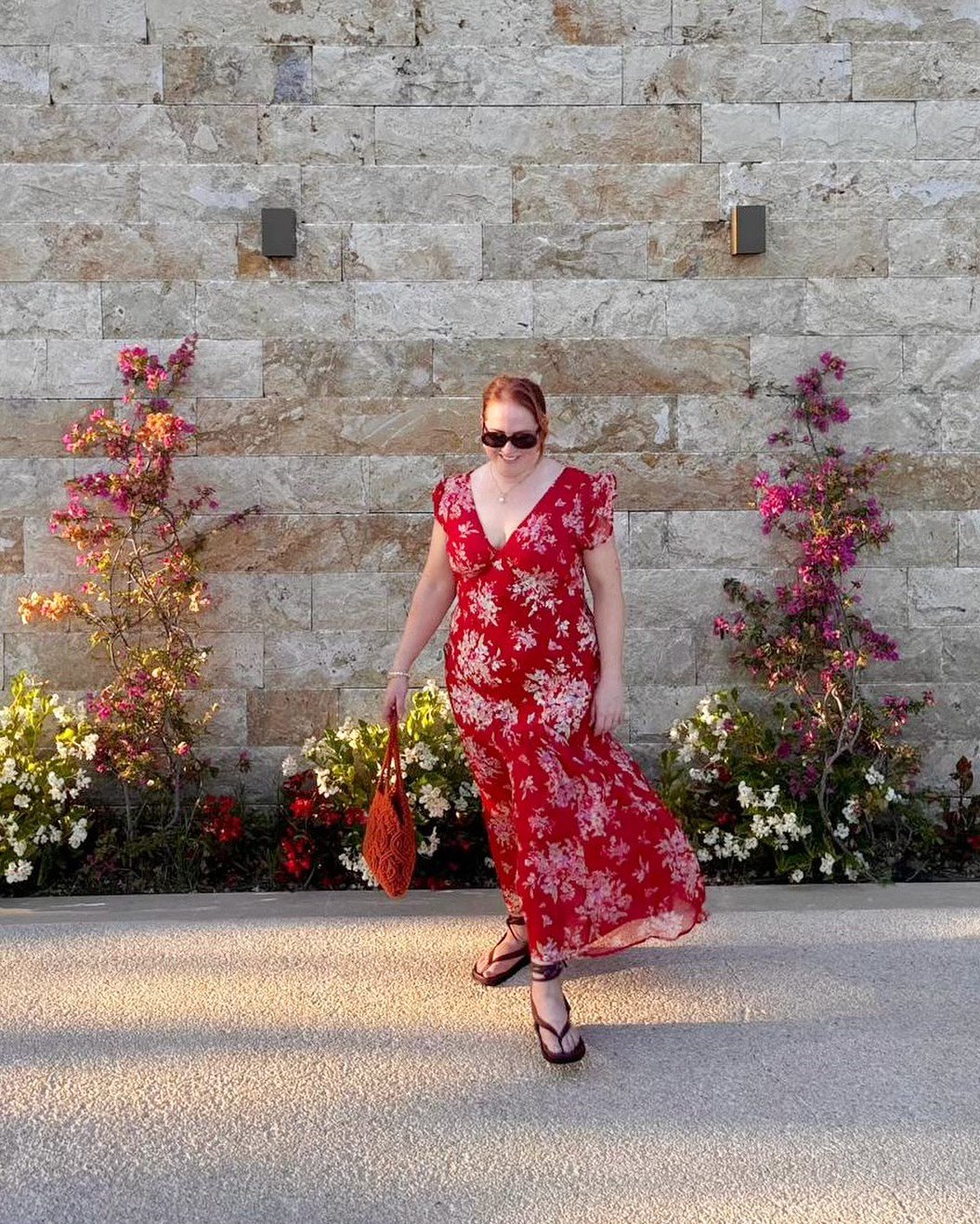Red Floral Flutter-Sleeve Maxi Dress with Woven Tote by a Textured Stone Wall