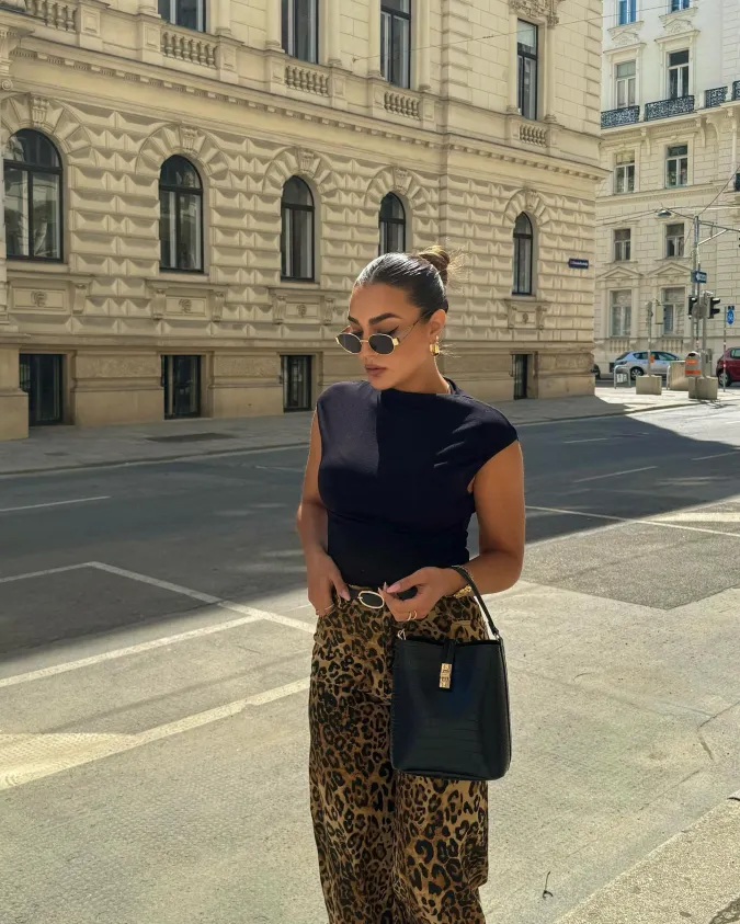 Sleeveless Black Top with Leopard Trousers and Structured City Bag Against Ornate Architecture